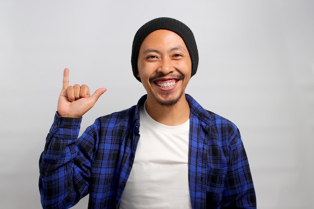 Il giovane asiatico sta facendo un gesto di roccia con la mano e un sorriso alla telecamera