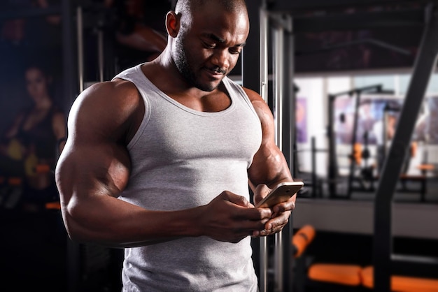 Il giovane atleta maschio utilizza il telefono durante un allenamento in palestra