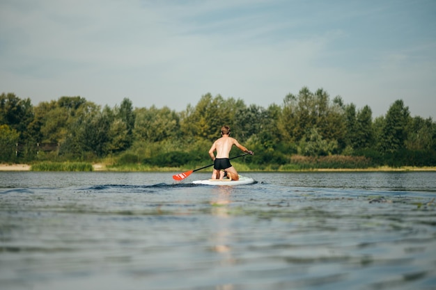 Il giovane atletico nuota lungo il fiume su una tavola da paddle vista dal retro