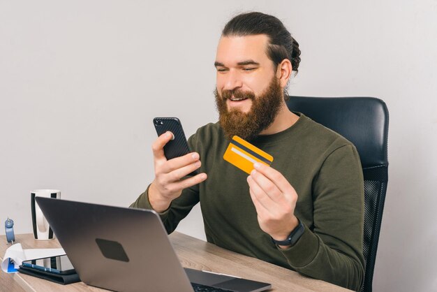 Il giovane barbuto sta usando la sua carta di credito e il suo telefono.