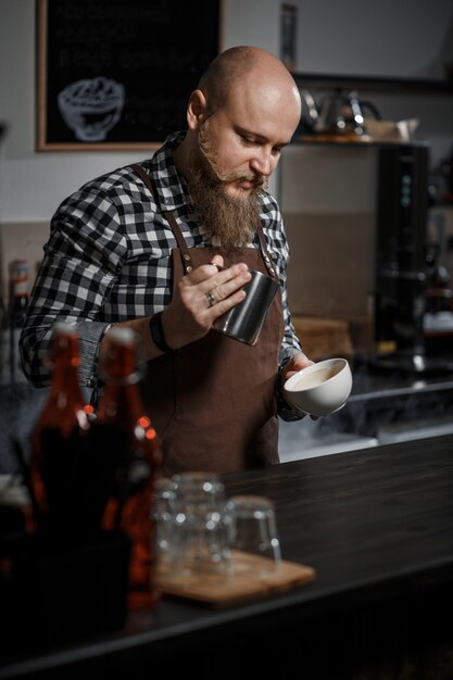 Il giovane barista in un grembiule fa il caffè al bar in un moderno caffè