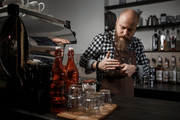 Il giovane barista in un grembiule fa il caffè al bar