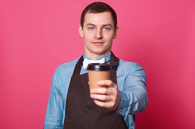 Il giovane barista maschio ti suggerisce una tazza di caffè fatta da lui, un papillon bianco e un grembiule marrone
