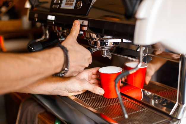 Il giovane barista prepara un delizioso caffè in una macchina da caffè professionale in un bicchiere di carta rosso