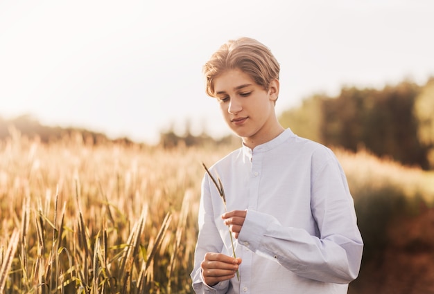 Il giovane bel ragazzo cammina su un campo di grano