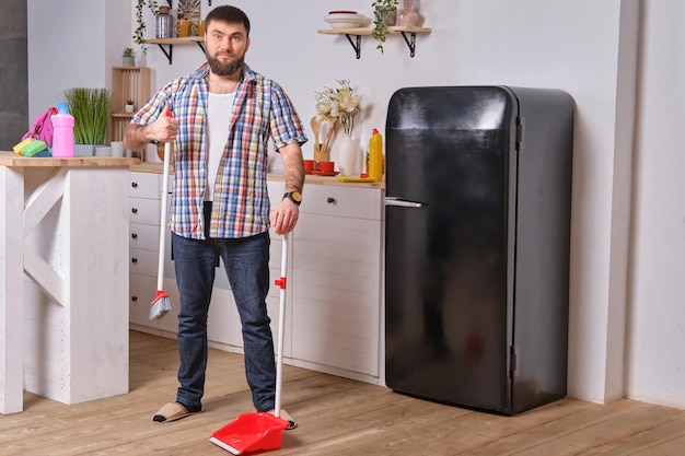 Il giovane bell'uomo barbuto in cucina che indossa una camicia a scacchi cerca di affrontare una paletta e un...