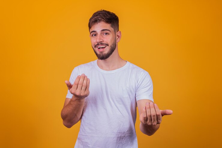 Il giovane bell'uomo caucasico che indossa una maglietta bianca su sfondo giallo che invita a venire con la mano ha un sorriso caloroso e un'espressione amichevole sul viso. felice che tu sia venuto