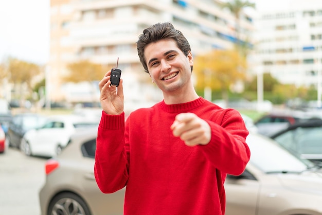 Il giovane bell'uomo con la chiave dell'auto ti punta il dito contro con un'espressione sicura