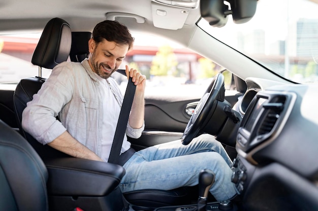 Il giovane bello felice che guida l'automobile allaccia la cintura di sicurezza