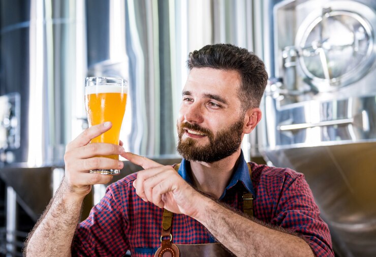 Foto il giovane birraio che indossa un grembiule di pelle sta testando la birra in un moderno birrificio