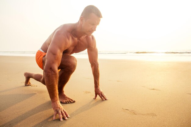 Il giovane bodybuilder maschio brutale mostra il torso forte della figura atletica al tramonto sull'esercizio di formazione dei pugili sexy della spiaggia