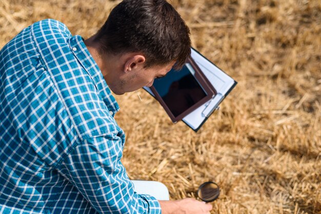 Il giovane botanico agronomo studia il fieno falciato con la lente d'ingrandimento e una compressa nel campo