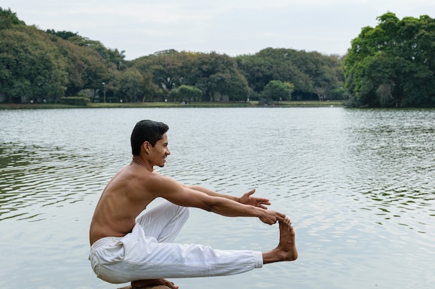 Il giovane brasiliano si è accovacciato accanto a un lago, a torso nudo, allungando una gamba e un braccio.