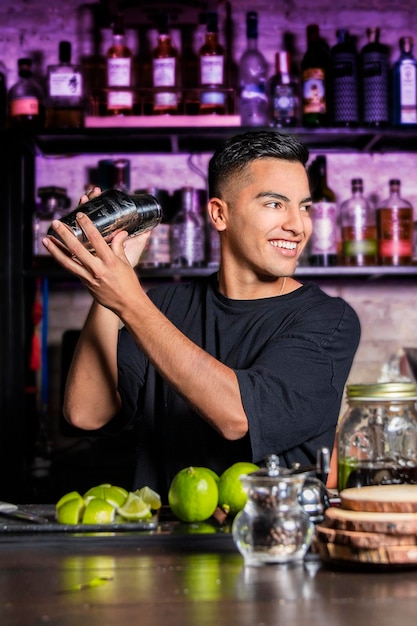 Il giovane cameriere latinoamericano con uno shaker guarda di lato sorridendo