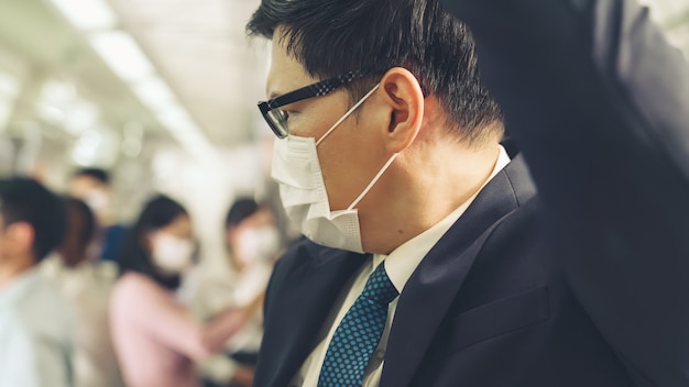Il giovane che indossa la maschera per il viso viaggia su un treno della metropolitana affollato