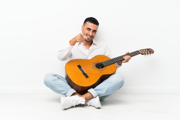 Il giovane che si siede sul pavimento con la chitarra indica il dito con un'espressione sicura