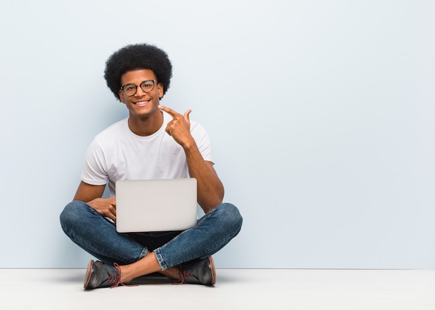 Il giovane che si siede sul pavimento con un computer portatile sorride, indicando la bocca