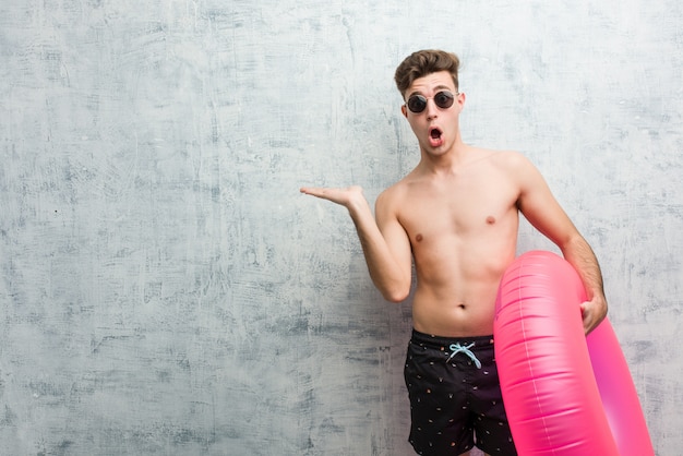 Il giovane che tiene una ciambella gonfiabile rosa che indossa un costume da bagno ha impressionato la tenuta dello spazio della copia sul palmo.