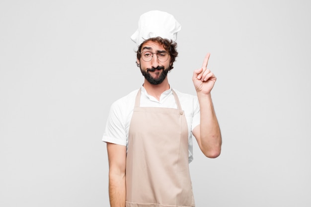 Il giovane chef pazzo si sente come un genio che tiene orgogliosamente il dito in aria dopo aver realizzato una grande idea, dicendo Eureka contro il muro bianco