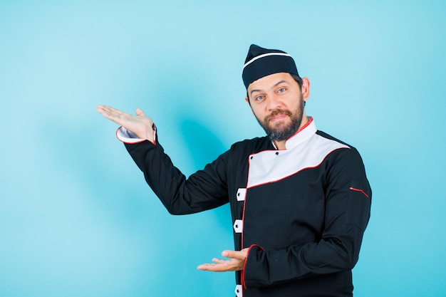 Il giovane chef sta guardando l'acmera alzando la mano su sfondo blu