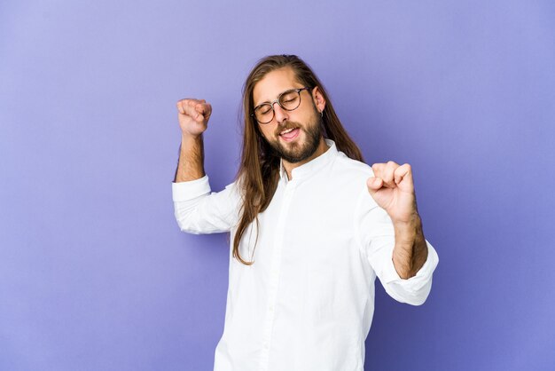 Il giovane con i capelli lunghi guarda un giorno speciale, salta e alza le braccia con energia.