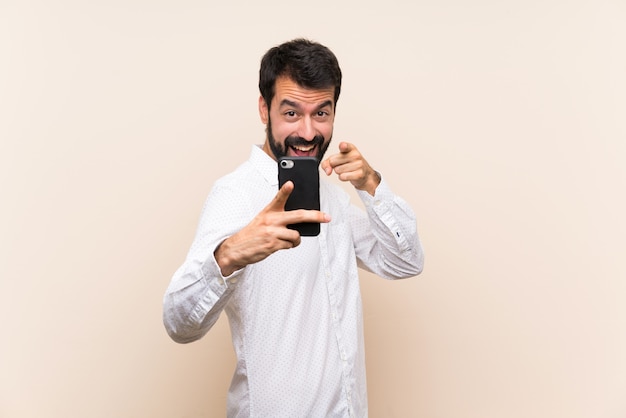 Il giovane con la barba che tiene un cellulare indica il dito mentre sorride