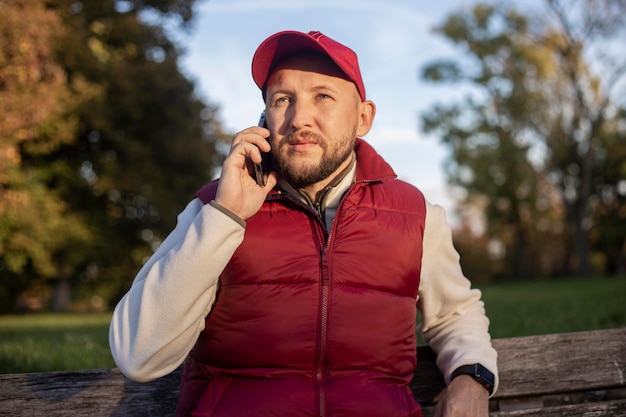 Il giovane con la barba parla al telefono mentre è seduto su una panchina