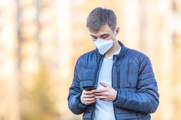 Il giovane con la maschera protettiva sul viso comunica dal telefono cellulare. Concetto di coronavirus Covid-19.
