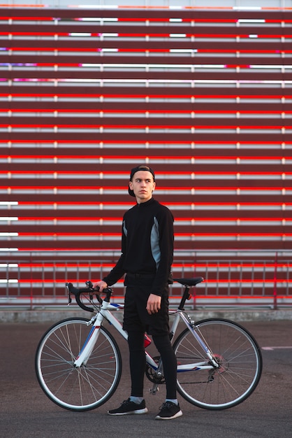 Il giovane con una bicicletta e un vestito atletico è su un fondo rosso astratto.