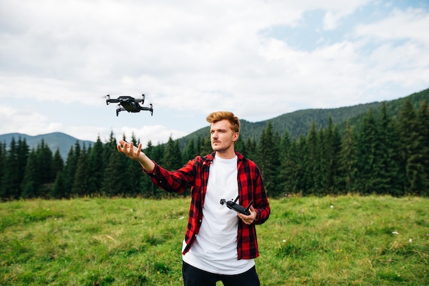 il giovane con una camicia rossa si trova su un prato di montagna su un drone controlla con un telecomando