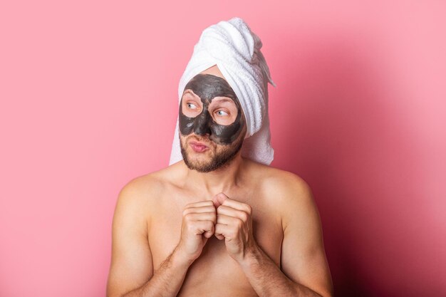 Il giovane con una maschera cosmetica nuda guarda di lato su uno sfondo rosa