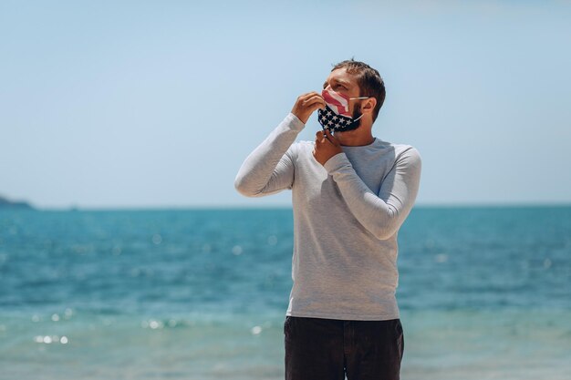 Il giovane con una maschera medica nel colore della bandiera americana che lo protegge dal virus sta posando e toccando la maschera con le mani. Concetto di problema globale.