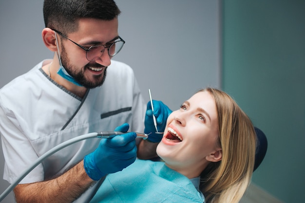 Il giovane dentista allegro sta nella sala e nel trattamento dei denti