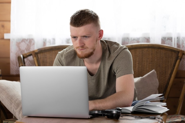 Il giovane di pensiero attraente lavora con il computer portatile, comunica nei social network