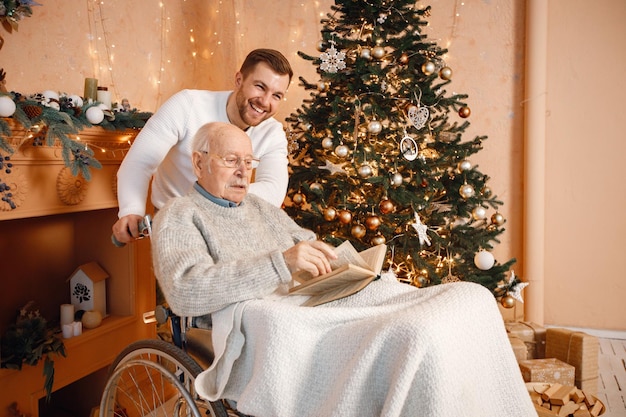 Il giovane e il suo vecchio padre su una sedia a rotelle seduti vicino all'albero di Natale