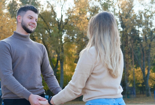 Il giovane e la donna si tengono per mano e si guardano l'un l'altro Ragazzo e ragazza che posano sullo sfondo di alberi autunnali