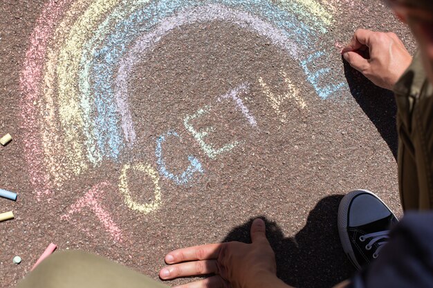 Il giovane è seduto su un marciapiede e disegna un arcobaleno