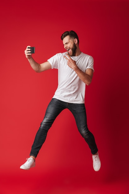 Il giovane eccitato fa selfie dal telefono cellulare che salta.