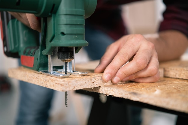 Il giovane falegname taglia una scheda osb con un seghetto alternativo artigiano mani in stoffa guanti protettivi puzzle