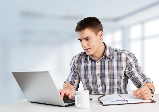 Il giovane felice lavora sul suo computer portatile con il caffè al tavolo