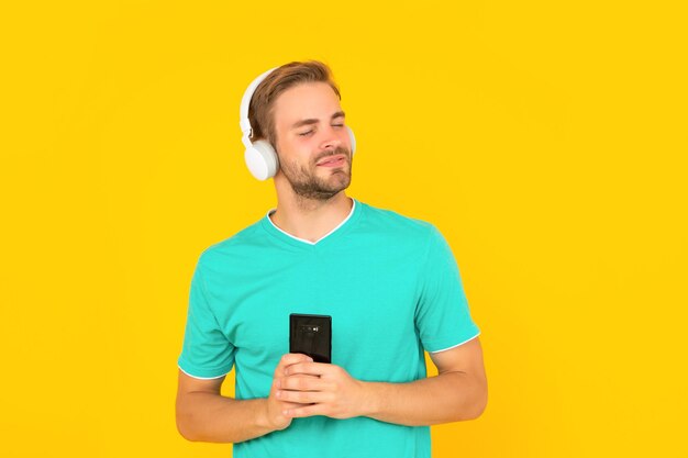 Il giovane felice si diverte ad ascoltare la musica sul telefono cellulare con lo sfondo giallo delle cuffie, per il tempo libero