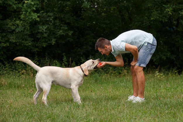 Il giovane felice sta addestrando un cane Labrador all'aperto