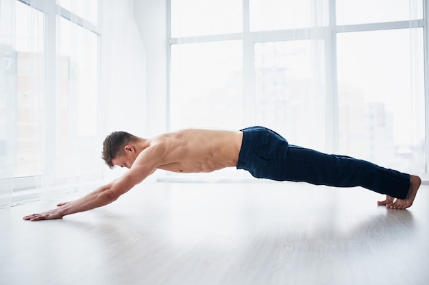 Il giovane forte uomo senza camicia pratica l'yoga allo studio di yoga