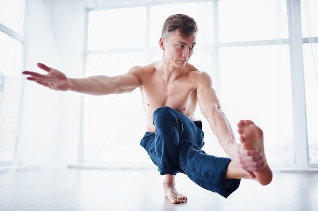 Il giovane forte uomo senza camicia pratica l'yoga allo studio di yoga