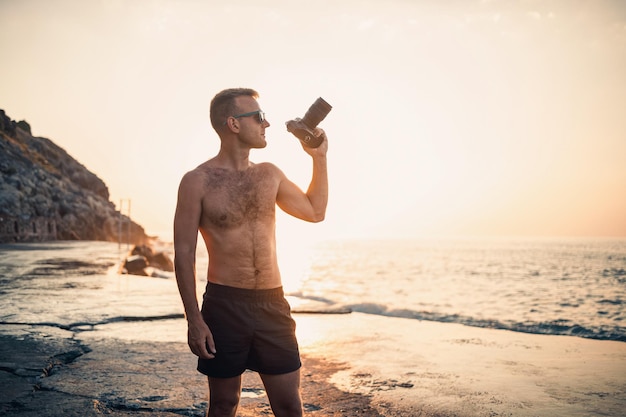 Il giovane fotografo maschio fa fotografie del mare al tramonto mentre si trova sulla riva Tramonto sul mare Messa a fuoco selettiva Turista fotografa il paesaggio marino