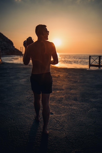 Il giovane fotografo maschio fa fotografie del mare al tramonto mentre si trova sulla riva Tramonto sul mare Messa a fuoco selettiva Turista fotografa il paesaggio marino