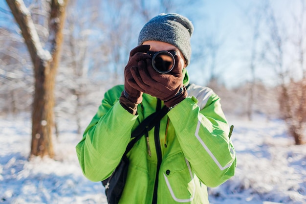 Il giovane fotografo scatta foto della foresta invernale utilizzando la fotocamera Giovane uomo che scatta foto all'aperto