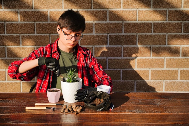 Il giovane giardiniere trapianta i fiori in un nuovo vaso Strumento per piantare terreno e drenaggio Hobby è il giardinaggio domestico