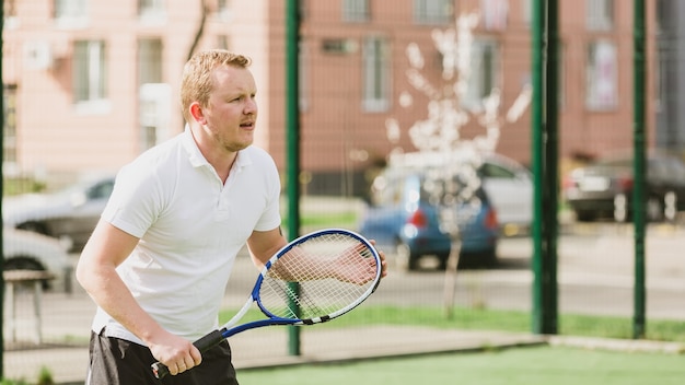 Il giovane gioca a tennis all'aperto sul campo da tennis al mattino presto