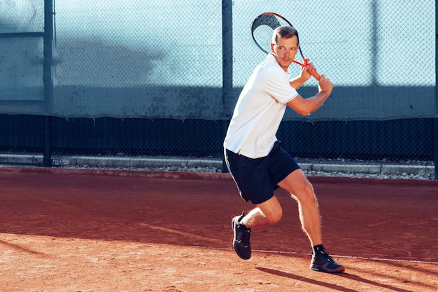 Il giovane gioca a tennis all'aperto sul campo da tennis al mattino